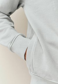 Lysegrå sweatshirt med ribbede manchetter og lomme, lavet af tekstureret stof med en afslappet pasform og minimale syninger.