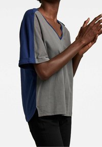 Szara i granatowa koszulka V-neck z krótkimi rękawami, wykonana z miękkiego materiału. Boczny rozcięcia i kontrastowe wykończenia rękawów dodają wizualnego zainteresowania.