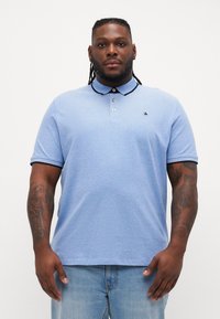 Lichtblauw poloshirt met een kraag, korte mouwen en een zwarte rand. Bevat een klein geborduurd logo op de linkerkant van de borst.