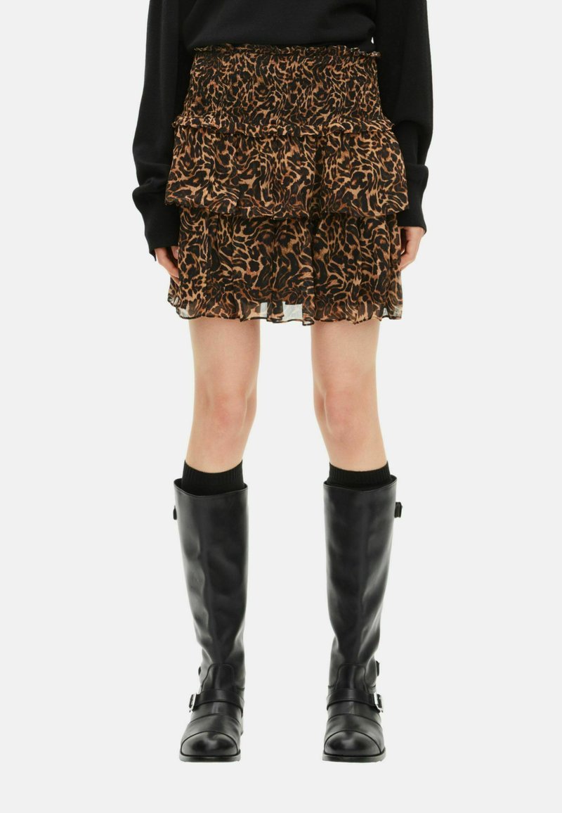 Mini falda en capas y con volantes en marrón con un estampado de leopardo. Combinada con botas negras hasta la rodilla y una blusa negra de manga larga.