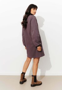 Robe-sweat en violet avec des manches longues, des épaules tombantes et un bas ourlé. Associée à des bottes chevilles à imprimé léopard et des chaussettes côtelées.