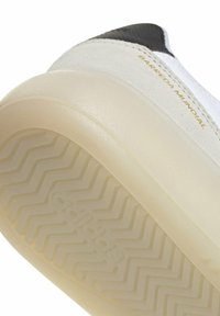 Gros plan sur la semelle en caoutchouc translucide et le talon d'une basket blanche et noire avec le texte "BARREDA MUNDIAL" sur la tige.