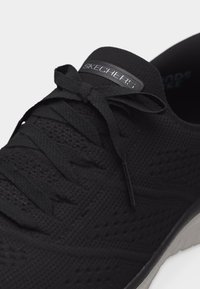 Μαύρο αθλητικό παπούτσι Skechers με πλεκτό επάνω μέρος, δέσιμο κορδονιών και επενδεδυμένη γκρι σόλα σε κοντινό πλάνο.