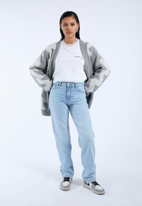 Cárdigan gris claro con un patrón de zigzag sobre una camiseta blanca, combinado con jeans azul claro y zapatillas negras y grises.