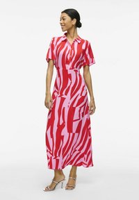 Vestido midi a rayas rojas y rosas con mangas cortas, cierre de botones en la parte delantera y un corte relajado, combinado con sandalias de tacón plateadas. Textura suave.