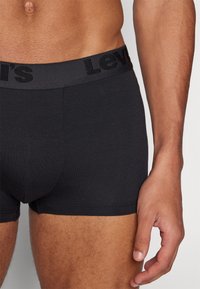 Schwarze Baumwollboxershorts mit breitem, elastischem Taillenbund, der den eingeprägten Markennamen zeigt. Glatte Textur und enganliegendes Design.