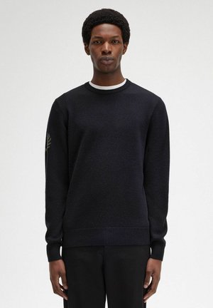 Maglione da uomo nero a girocollo in maglia testurizzata, con colletto interno bianco e dettaglio del logo ricamato verde sulla manica sinistra.