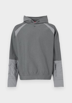 Hall halliga kapuutsiga dressipluus halli tekstuurse kere, raglaanvarrukatega, esitasku ja külgedel luku detailiga. Rinnal on must logo.