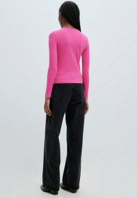 Haut moulant à manches longues en maille côtelée rose vif, associé à un pantalon noir taille haute à jambes larges et des bottines noires.