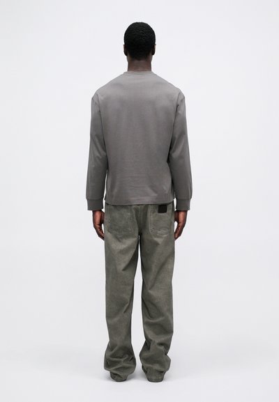 Pelēks garām piedurknēm krekls ar ribota stila aprocēm, apvienots ar vaļīgām zaļām biksēm. Audums izskatās mīksts; minimāls dizains un aizmugures logotipa detaļa.