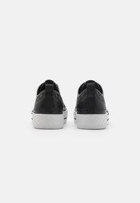 Schwarze Sneaker mit strukturiertem Obermaterial, niedrigem Design, kontrastierender weißer Sohle und einer Lasche hinten für einfaches Anziehen.