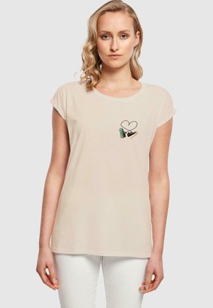 Lys beige bomulds T-shirt med korte opsmøgede ærmer, en rund halsudskæring, og et lille broderet design med et hjerte og fodtøj.