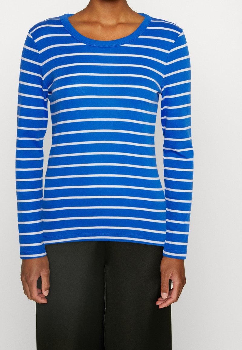 Blå långärmad skjorta med horisontella vita ränder, rund halsringning, smal passform och mjuk textur. Kombinerad med svarta byxor.