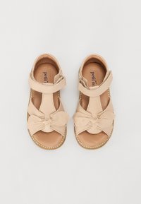 Sandales en cuir beige clair avec un détail en nœud, bout ouvert et sangle ajustable. Semelle intérieure douce et bords cousus pour la durabilité.