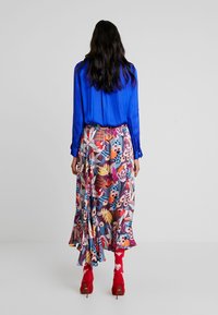 Zwiewna kwiecista spódnica w żywych kolorach, z motywem liści, w połączeniu z kobaltową bluzką. Uzupełniona czerwonymi szpilkami i skarpetkami.