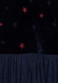 Zwart fluwelen stof met rode en donkergrijze sterrenborduursels, met een geplooide marineblauwe tule onderkant. Soepele textuur en rijke kleuren.