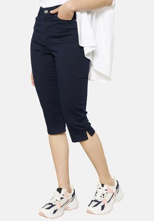 Navy blue cropped pants with a fitted design, side slits at the hem, paired with white and pink sneakers featuring a geometric pattern.