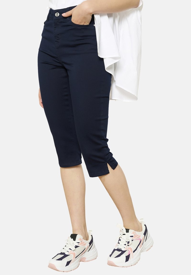 Pantaloni cropped blu navy con un design aderente, fessure laterali all'orlo, abbinati a sneakers bianche e rosa con un motivo geometrico.