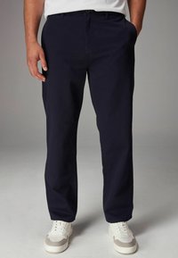 Pantalons bleu marine avec une coupe droite, dotés d'un devant plat, de deux poches latérales et portés avec des baskets blanches et grises.