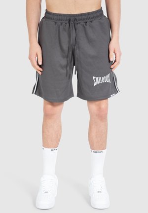 Grå atletiske shorts med ribbet tekstur, en elastisk talje, et hvidt logo og kontrasterende sidelister. Kombineret med hvide sneakers og sokker.