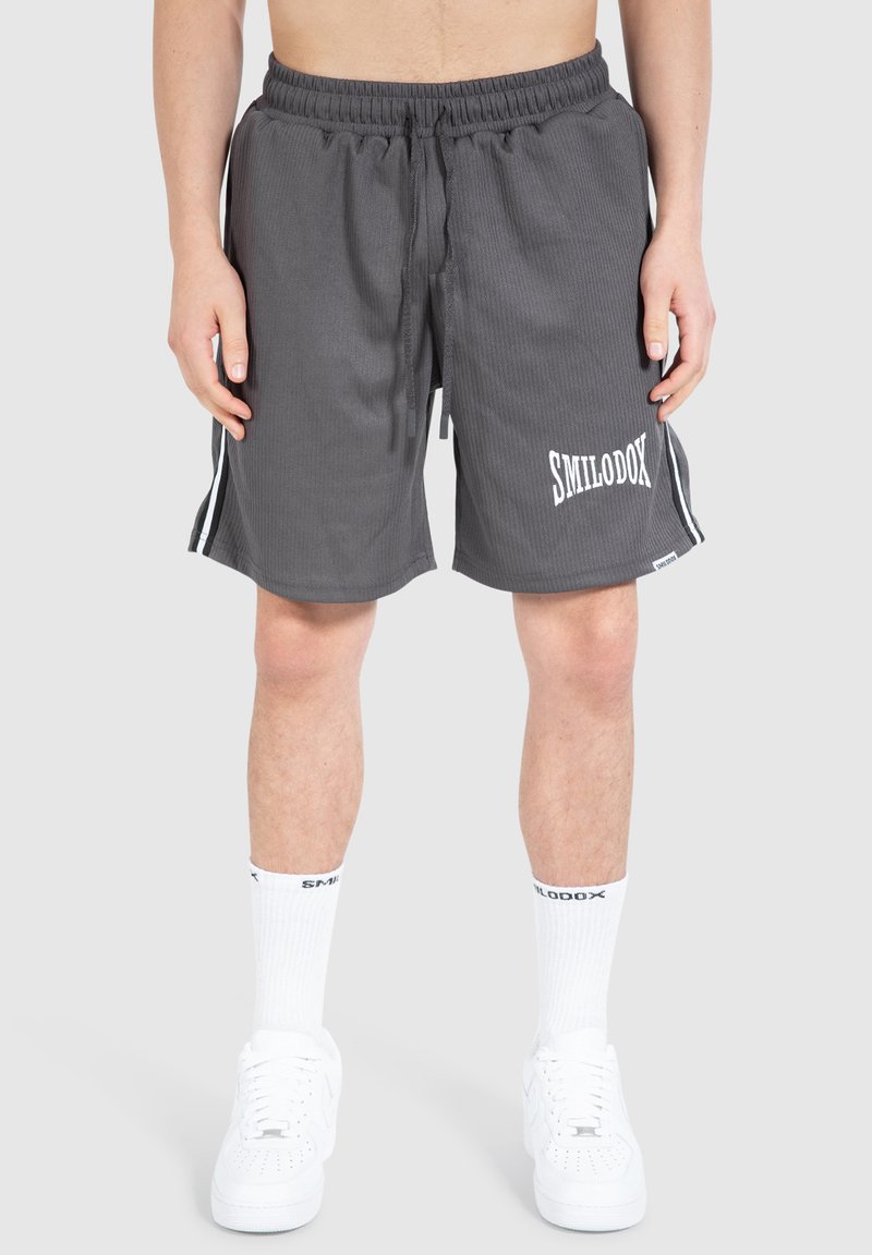 Graue Sportshorts mit gerippter Textur, elastischem Bund, weißem Logo und kontrastierenden Seitenstreifen. Kombiniert mit weißen Turnschuhen und Socken.
