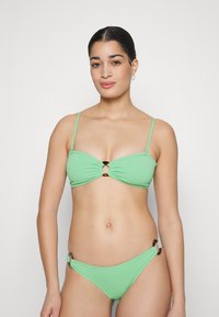 Bikini vert en tissu texturé, avec un design froncé et un accent circulaire au centre et sur les bretelles latérales.