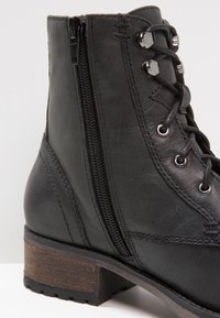 Botín de cuero negro con diseño de cordones, cremallera decorativa, acabado texturizado y tacón de bloque de madera con suela estampada.