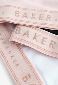 Svijetloružičaste trake od tkanine s "BAKER" izbočenim, reflektirajućim slovima. Sadrži sjajnu niti kao naglasak duž rubova.