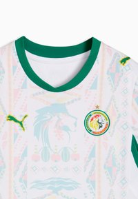 Wit sportshirt met groene kraag, Puma-logo, embleem van de Senegalese voetbalbond en subtiele kleurrijke tribale patronen.