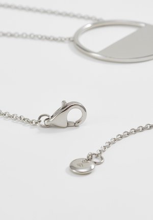 Chaîne de collier en argent avec fermoir mousqueton et pendentif géométrique reposant sur une surface blanche.