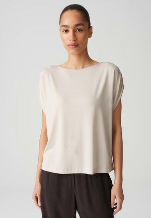 Licht beige t-shirt met korte mouwen en een wijde halslijn, gemaakt van zachte stof. Het heeft een relaxed fit en een gladde textuur. Gecombineerd met donker gestructureerde broek.