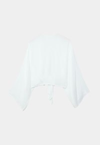 Blouse blanche courte avec de larges manches fluides et un détail noué dans le dos, présentée à plat sur un fond clair.