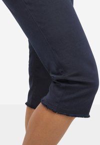 Pantalons en denim bleu marine courts avec des détails à bords bruts et une texture lisse, présentant une coupe ajustée qui épouse la jambe.
