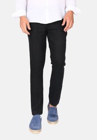 Dunkle, schmal geschnittene Hosen aus leichtem Stoff mit glatter Textur. Getragen mit blauen Schuhen und einem weißen Langarmhemd.