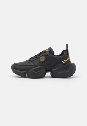 Czarne masywne sneakersy z grubą podeszwą, złotymi logo Versace Jeans Couture na pięcie, języku i boku oraz teksturowanymi detalami na śródpodeszwie.