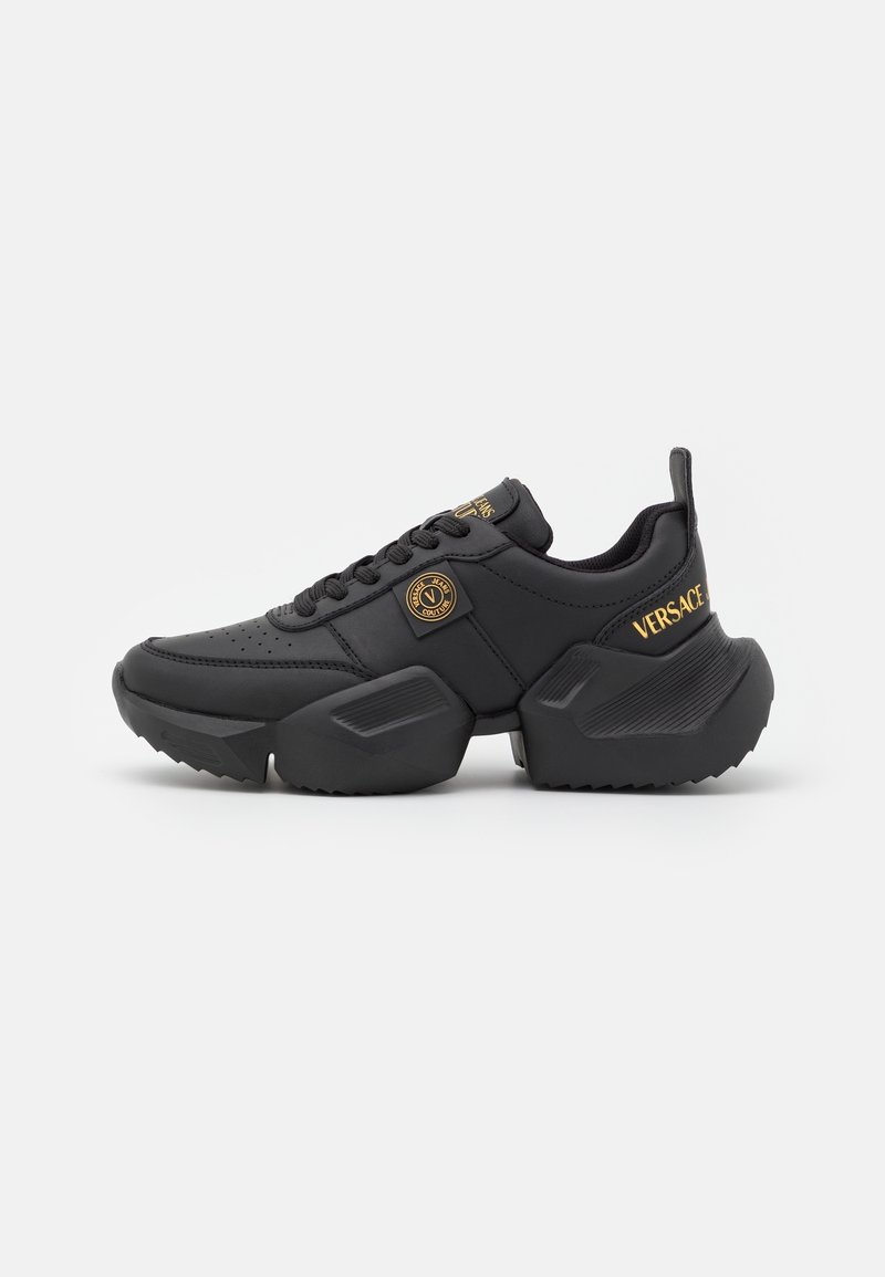Baskets noires épaisses avec une semelle épaisse, logos Versace Jeans Couture dorés au talon, sur la languette et sur le côté, avec des détails texturés sur la semelle intermédiaire.
