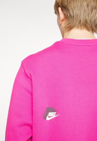 Magenta sweatshirt featuring a round neck and short sleeves. Includes a white Nike logo on the back, textured fabric with a smooth finish.