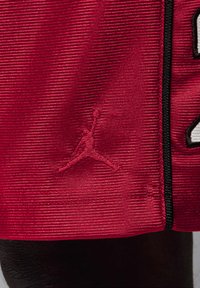 Crvena atletska majica s teksturiranim materijalom, izvezenim Jumpman logotipom i kontrastnim crnim obrubima duž rubova. Ima odvažne bijele brojke.