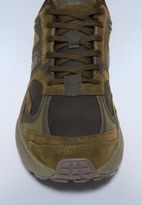 Zapatillas de deporte verde oliva con materiales de ante y malla, que presentan una puntera redonda, lengüeta acolchada, cordones gruesos y suela de goma texturizada.
