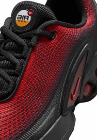 Zapatilla deportiva roja y negra con parte superior texturizada, lengüeta de malla y logo circular. Presenta un notable sistema de amortiguación Air Max en la suela.