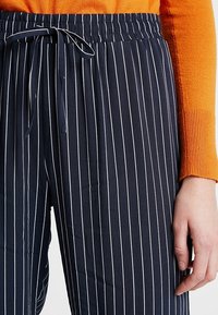 Niebieskie w pionowe paski spodnie z elastycznym pasem i białymi pionowymi liniami, wykonane z miękkiego materiału. Połączone z pomarańczowym swetrem z prążkowanej dzianiny.