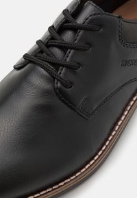 Scarpa in pelle nera con superficie texturizzata, caratterizzata da lacci neri e un bordo cucito. Include un discreto dettaglio di branding sul lato.