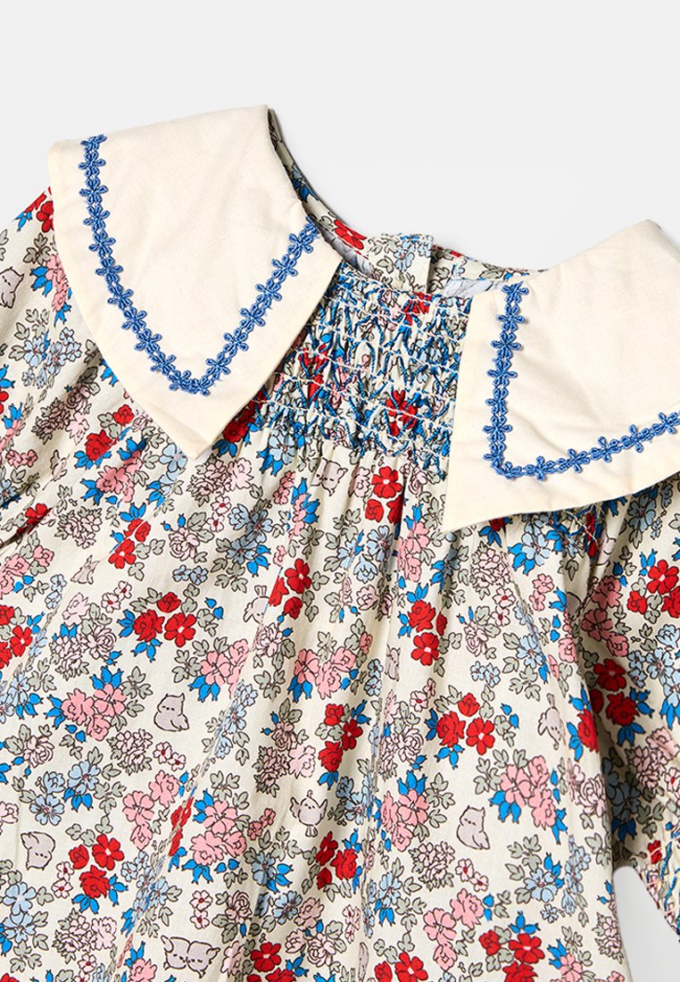 Blumenmusterkleid aus leichtem Stoff mit einem cremefarbenen, bestickten Kragen. Es hat kleine rote, rosa und blaue Blumenmuster mit Rüschendetails.