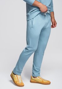 Lichtblauwe joggingsbroek van zachte stof met een trekkoord in de taille, gecombineerd met gele en witte sneakers met groene accenten.