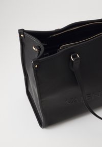 Črna usnjena torba s teksturiranim zaključkom, zlatimi zadrgami in vgraviranim logotipom. Ima več predelkov in nastavljive naramnice.