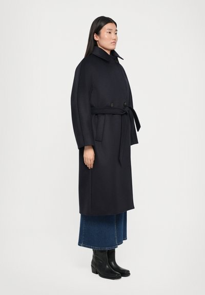 Navy wool blend coat with a belted waist, oversized collar, and button closure. Paired with a denim skirt and black ankle boots.