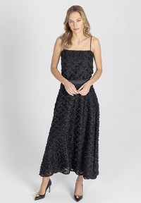 Czarna wieczorowa sukienka z kwiatowym wzorem, z cienkimi ramiączkami i dopasowaną talią. Posiada zwiewną spódnicę. Noszona z czarnymi butami na wysokim obcasie.