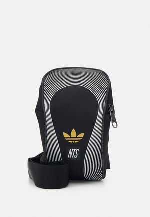 Zwarte crossbodytas met witte gebogen lijnen, gouden Adidas trefoil-logo, witte NTS-tekst en verstelbare band met rits aan de zijkant.