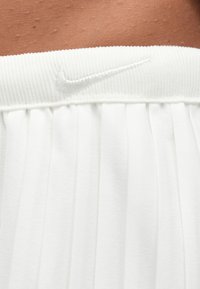 Tissu blanc plissé avec une ceinture côtelée comportant un logo Nike blanc brodé sur une peau bronzée.