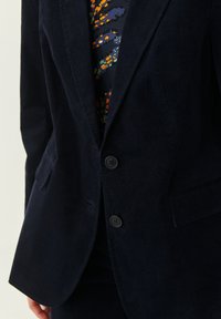 Námořnický tvídový blazer se dvěma knoflíky, klopovými límci a bočními kapsami; texturovaná tkanina s jemným žebrováním.